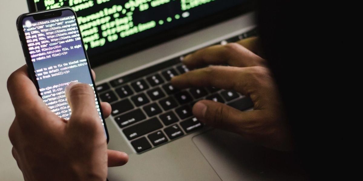 Free Unrecognizable hacker with smartphone typing on laptop at desk Stock Photo