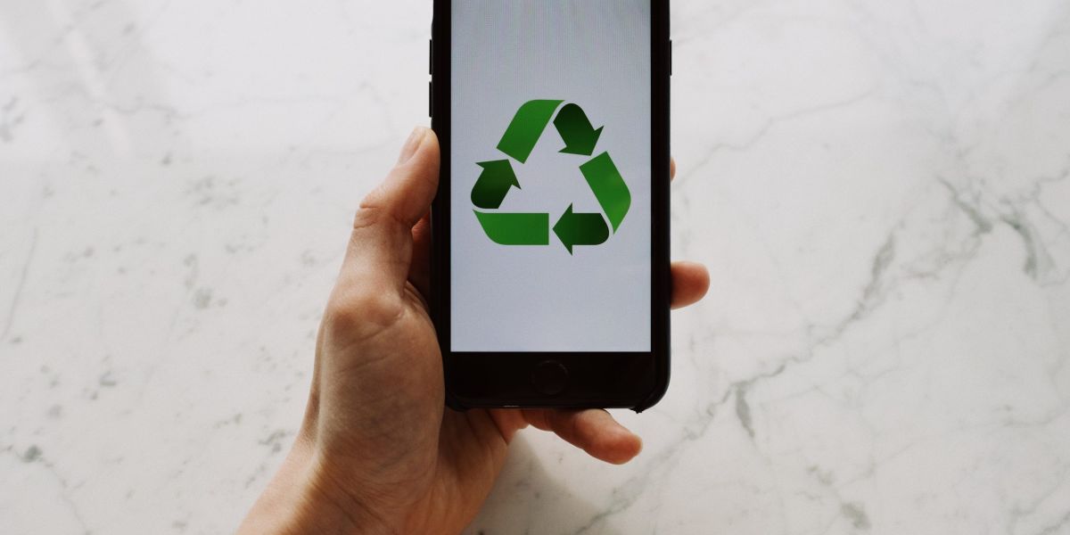 From above view of faceless person holding mobile phone with white screen and green recycle logo above marble surface