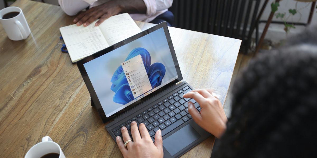 Overhead view of two people at a table working with a Microsoft laptop and notebook